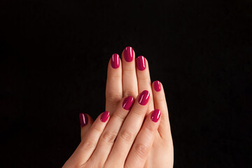 Female hands with beautiful manicure - viva magenta, pink nails on dark black background. Nail, skin care concept