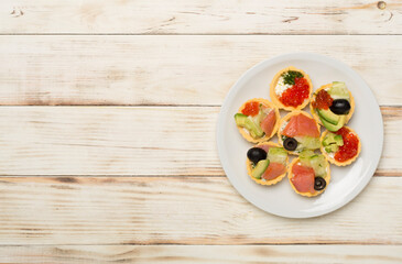 Tartlets with salmon and caviar on wooden background, top view