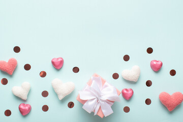 Background of knitted hearts, gift and confetti on a light blue background for Valentine's Day.