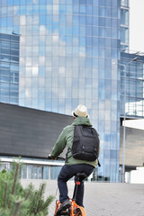 A man biking to work. Employee rides a bike to work in the office. Back view of a cyclist against the backdrop of an office building.