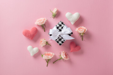 Minimalistic background for Valentine's Day. A banner layout with a knitted heart and a gift and roses on a light pink background with a space for text.