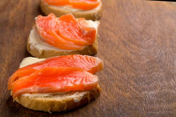 Toasts with red trout and butter on a board on a wooden table.