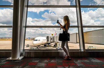 A woman takes photos on her phone at an airport