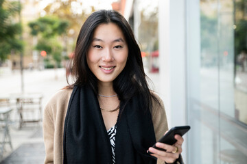 Beautiful woman smiling with a smartphone in the city - portrait of a young happy woman looking at camera