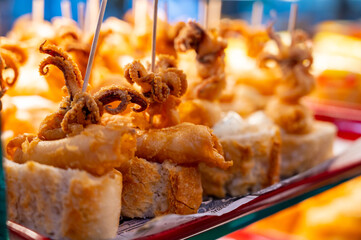 Fototapeta premium Typical snack of Basque Country, pinchos or pinxtos skewers with small pieces of bread, sea food, baby octopus, cheese, jamon served in bar in San-Sebastian or Bilbao, Spain