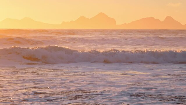 Sunrise over Stormy Sea. Shining Golden Waves with Sun Reflection at Sunset. Amazing light over Icelandic Coastline. Sharp Volcanic Cliffs. Atlantic Ocean Water. Iceland. Shot in 8K Resolution 4320p