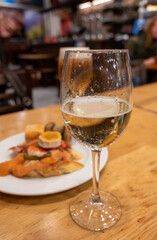 Board with typical snacks of Basque Country, pinchos or pinxtos, skewers or small piece of bread with toppings, served with glass of txakoli wine in bar in San-Sebastian or Bilbao, Spain