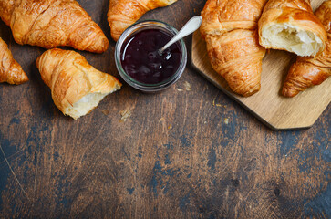 Freshly baked croissants with jam on dark wooden background. Top view, flat lay, copy space.