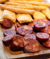 Wooden plate with sliced Spanish tapas, choriso sausage, lomo iberico en bread sticks