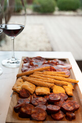 Wooden plate with sliced Spanish tapas, choriso sausage, lomo iberico en bread sticks served with glass of red wine