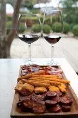 Wooden plate with sliced Spanish tapas, choriso sausage, lomo iberico en bread sticks served with glass of red wine