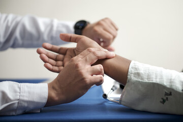 hands of unrecognizable doctor looking at his watch and feeling radial pulse of patient