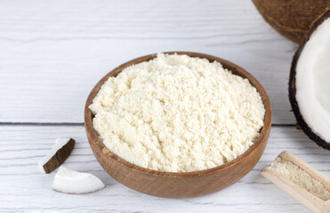 Coconut flour in a wooden bowl and fresh coconuts on a wooden background. Baking ingredients. Gluten free food.