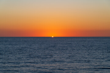 Just a sliver of sun remains under a colorful orange sky at sunset at the port of Cabo San Lucas, Mexico.