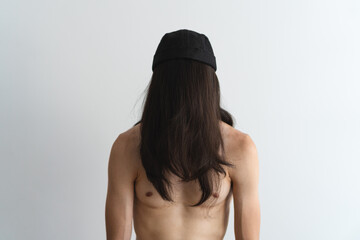 Young, athletic shirtless man with his face covered by his own hair wearing a brimless cap with a white background. Artistic photo.