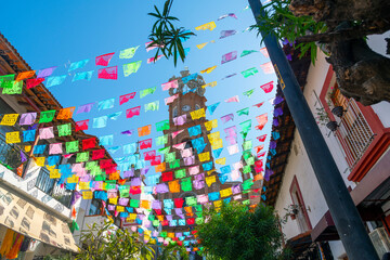 View from the street below of the The Church of Our Lady of Guadalupe with colorful flags strung across the street on a sunny morning in Puerto Vallarta, Mexico.