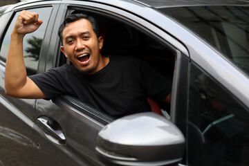 Happy asian driver showing his victory or success in his car with fist hand