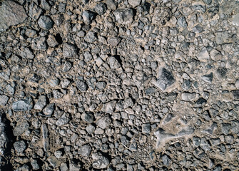 Dark grey cinder stones lie on a dirt road, top view in the rays of the midday sun.