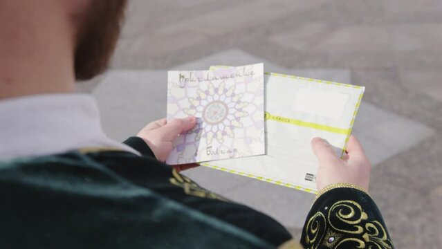 Person receives invitation to visit mosque in settlement Bolgar. Man wearing national clothes explores invitation in pretty envelope