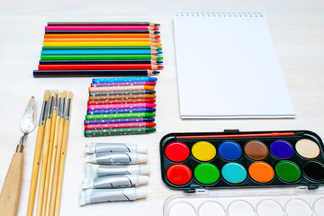 Naklejka premium Watercolor oil paints, paintbrushes, colorful pencils, pastel crayons,blank watercolor paper pad. Creativity creation process. Artist's stuff on white table.Top view Flatlay of drawing supplies