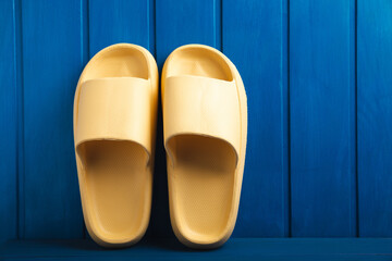 Yellow rubber summer slippers. Replacement shoes for home or office. Yellow slippers on a background of blue space. Relax concepts. Space for text.Space for copy.