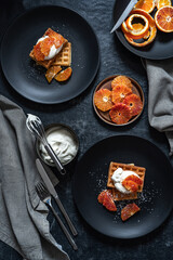 Belgian waffles with oranges and wippet cream. Served on a black table. Top view. Low key photography in rustic style.