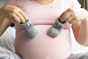 Pregnant woman holds two little wool booties on belly. Healthy pregnancy.