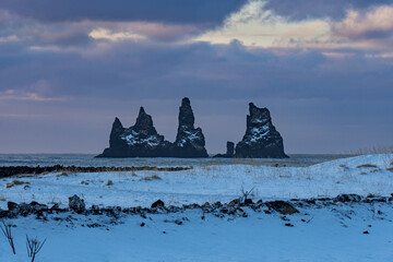 Black stones of Reynisfjara beach on the horizon of the black sand beach under a dramatic sky and totally snow covered ground - Powered by Adobe