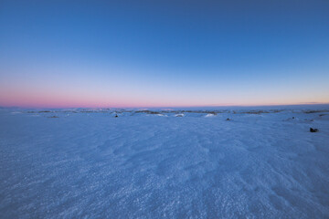 Flat landscape to the horizon covered in snow and illuminated by the magical purple colored...