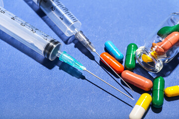 Medical syringes with ampule and pills on blue background, closeup
