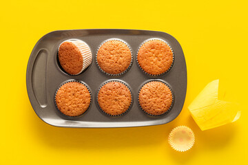 Baking tray with muffins and paper forms on yellow background