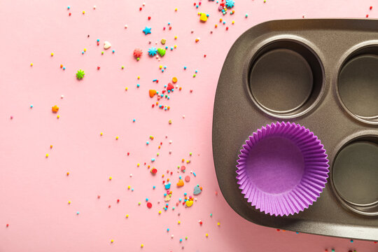 Muffin Baking Tray With Paper Form And Sprinkles On Pink Background