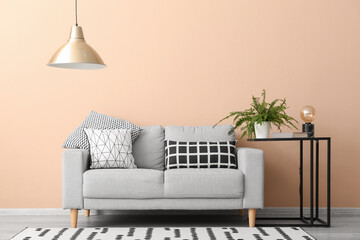 Table with houseplant, lamp, book and grey sofa near beige wall