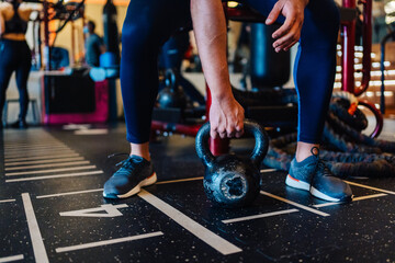 Young couple is working out at gym. Attractive woman and handsome muscular man are training in light modern gym. Doing plank on kettlebell. Push-up on weights.