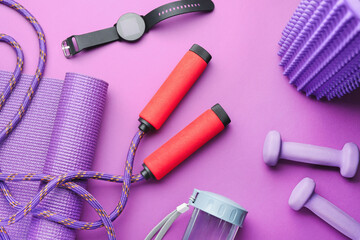 Skipping rope, mat, smartwatch, dumbbells and bottle on violet background