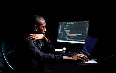 Black male reading code on laptop in a dark room