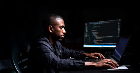 Black male coding in a dark room