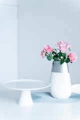 In the white kitchen on the table is an empty white tray for sweets and pink flowers in a vase - roses. Concept, interior, style, fashion, life, romance