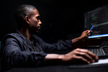 Black male checking code he wrote in a dark room