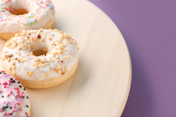 Wooden board with delicious donuts on color background, closeup