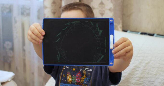The child shows the camera a drawing of a virus on a tablet that he drew. The child holds a tablet with a picture in his hands and shows it to the camera.
