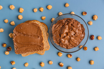 Composition with tasty toasts, bowl of hazelnut butter and nuts on color background