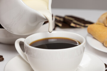 Cream from the milk jug is poured into coffee, making coffee with cream, cappuccino.