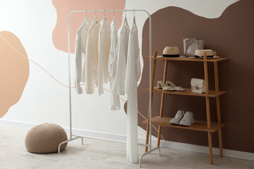 Rack with white clothes, shelving unit and accessories near color wall