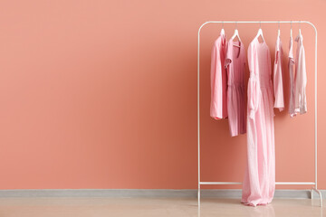 Rack with female clothes near pink wall