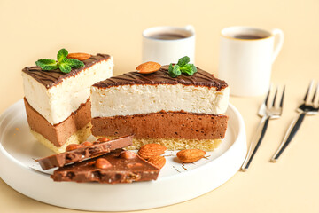 Plate with pieces of birds milk cake, chocolate, almond nuts, cups and forks on beige background