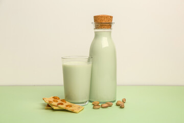 Glass and bottle of delicious pistachio milk and chocolate bars on green table near white wall