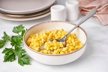 Bowl with canned corn, spoon and parsley on white table