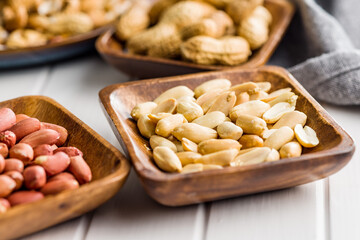 Unpeeled and peeled peanuts in bowl on kitchen table.