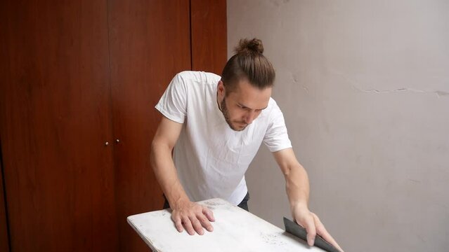 Young White Guy Sanding a Wooden Board in an Empty Room